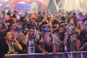 Energetic crowd at a music festival enjoying live performances with drinks.